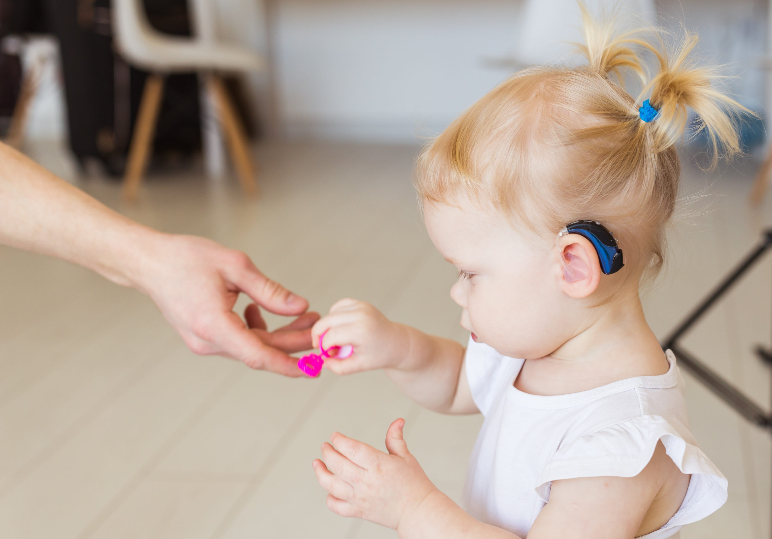 Hearing aid in baby girl's ear. Toddler child wearing a hearing aid at home. Disabled child, disability and deafness concept.